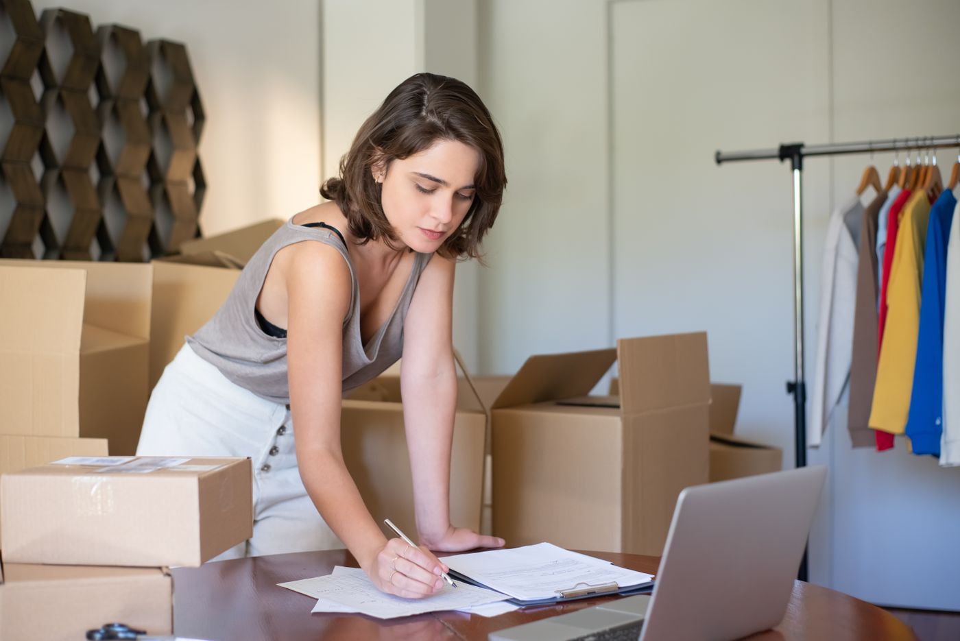 Gérante d'une boutique de mode en ligne, entourée de cartons d'expédition, gérant sa facturation sur ordinateur portable